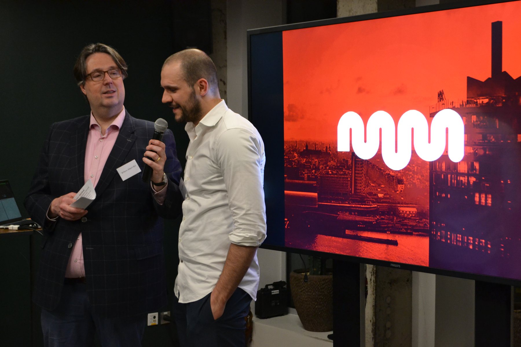 Twee heren met een microfoon voor een scherm met het logo van MassiveMusic